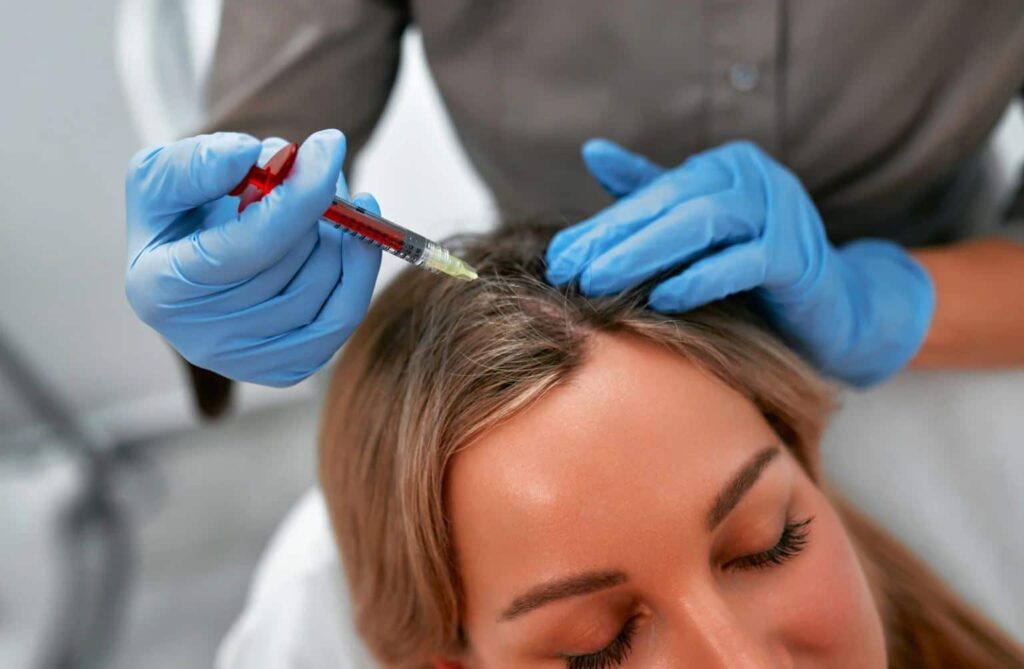 A healthcare professional in blue gloves performs a scalp treatment on a woman with light brown hair. The practitioner uses a syringe to inject a solution aimed at promoting hair growth or treating hair loss. The setting appears to be a modern clinic, emphasizing a clean and professional environment. This image highlights advancements in hair restoration techniques, appealing to individuals seeking solutions for thinning hair or alopecia.
