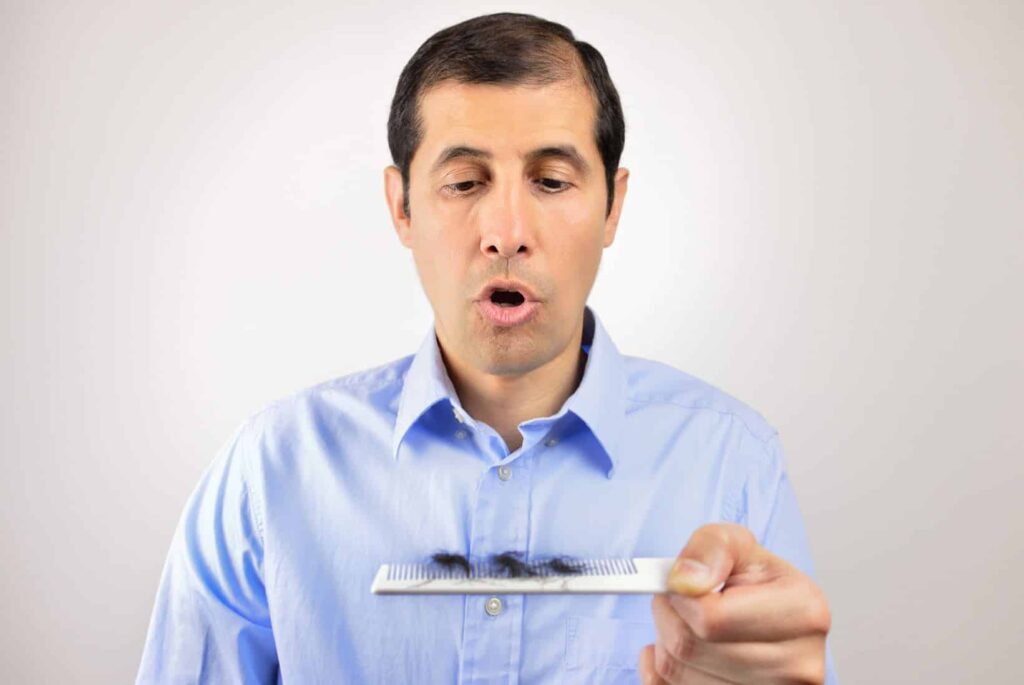 A man in a light blue shirt is surprised while holding a small object, possibly a science experiment. His mouth is open in astonishment, indicating a reaction to the object he is examining. The background is neutral, focusing attention on the man and the item. This image captures a moment of curiosity and discovery, ideal for educational content related to science or experiments.
