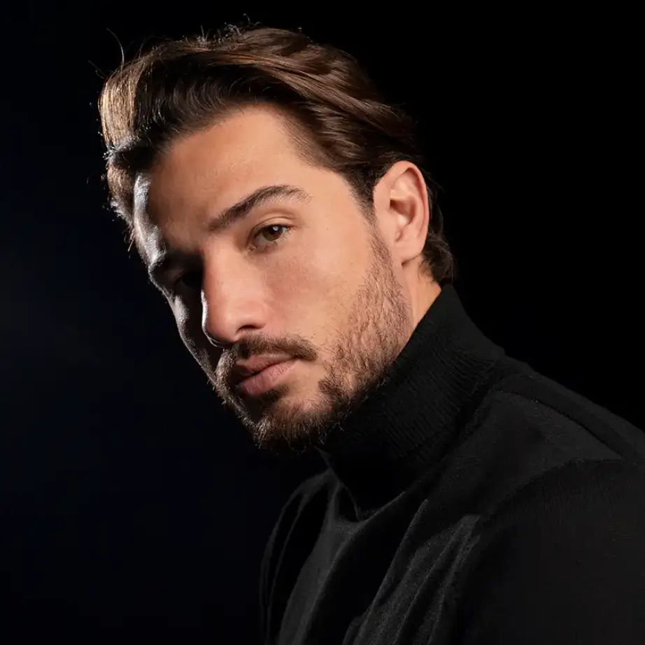 Portrait of a young man with styled brown hair, wearing a black turtleneck sweater. He is facing slightly to the side, with a serious expression, set against a dark background. The lighting highlights his facial features, creating a dramatic effect. This image conveys confidence and sophistication, suitable for fashion or personal branding contexts.