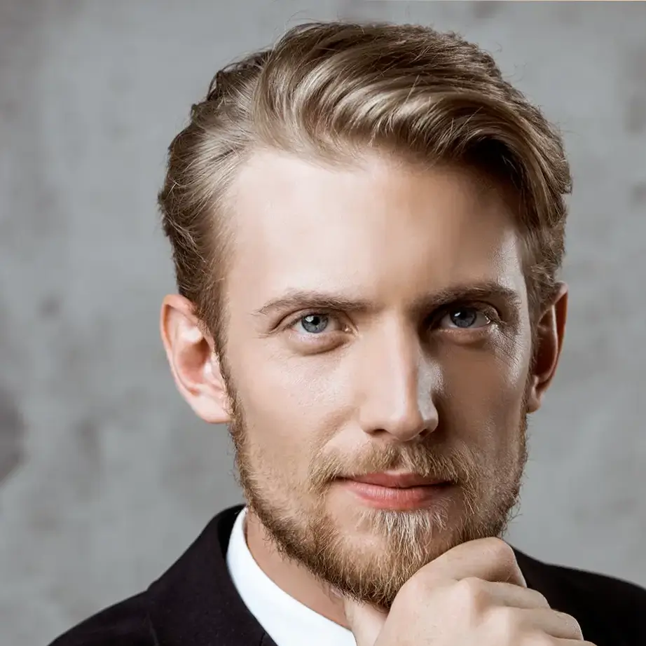 Portrait of a young man with light hair and a well-groomed beard, wearing a black suit. He is thoughtfully resting his chin on his hand, with a serious expression, against a textured gray background. The image conveys professionalism and confidence, making it suitable for business-related content or personal branding.