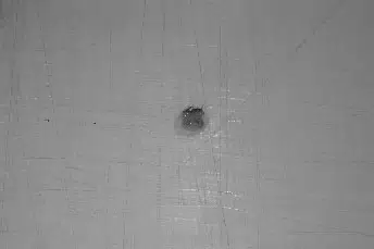 Close-up image of a small dark spot on a light-colored wall, highlighting a surface imperfection or damage. The spot appears to be a minor hole or blemish, with surrounding areas showing a smooth texture. This image can be useful for identifying wall repairs or maintenance needs in residential or commercial settings.
