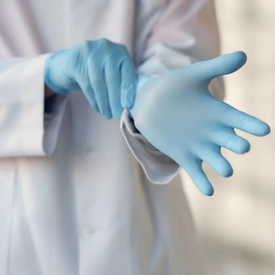 A healthcare professional wearing blue latex gloves prepares for a medical procedure. The individual is adjusting the gloves, indicating readiness for tasks that require hygiene and safety. This image highlights the importance of personal protective equipment in healthcare settings to prevent contamination and ensure patient safety.