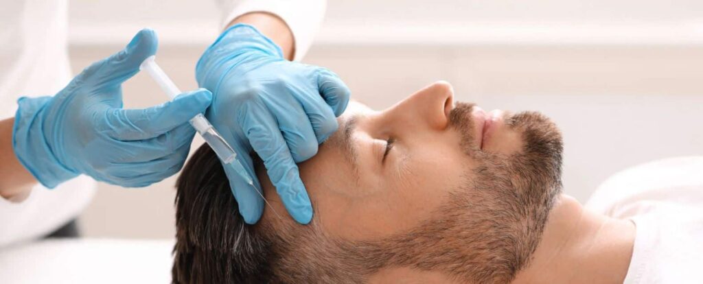 A healthcare professional wearing blue gloves administers a cosmetic treatment to a male patient in a clinical setting. The patient lies back with his eyes closed, indicating relaxation during the procedure. This image highlights the growing trend of non-surgical aesthetic procedures, emphasizing safety and professionalism in cosmetic treatments.